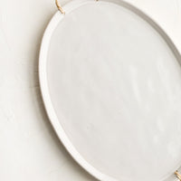 2: A glossy white ceramic platter in oval shape with rattan wrapped handles at sides.