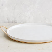 3: A glossy white ceramic platter in oval shape with rattan wrapped handles at sides.