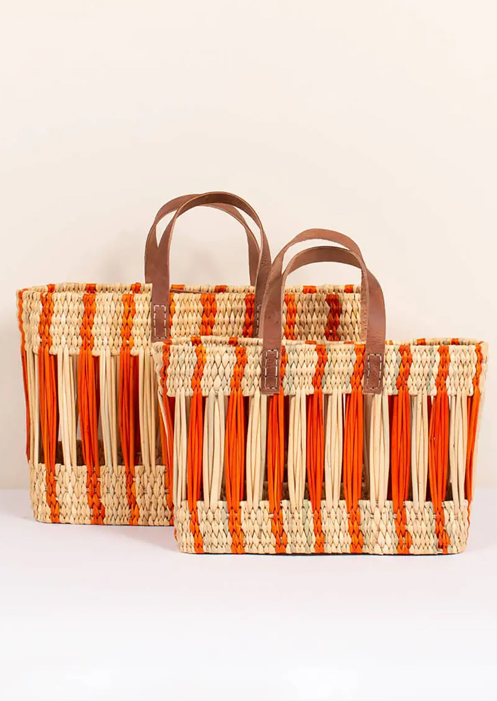 3: An oblong open weave basket in natural reed with bright orange stripes and brown leather handles.