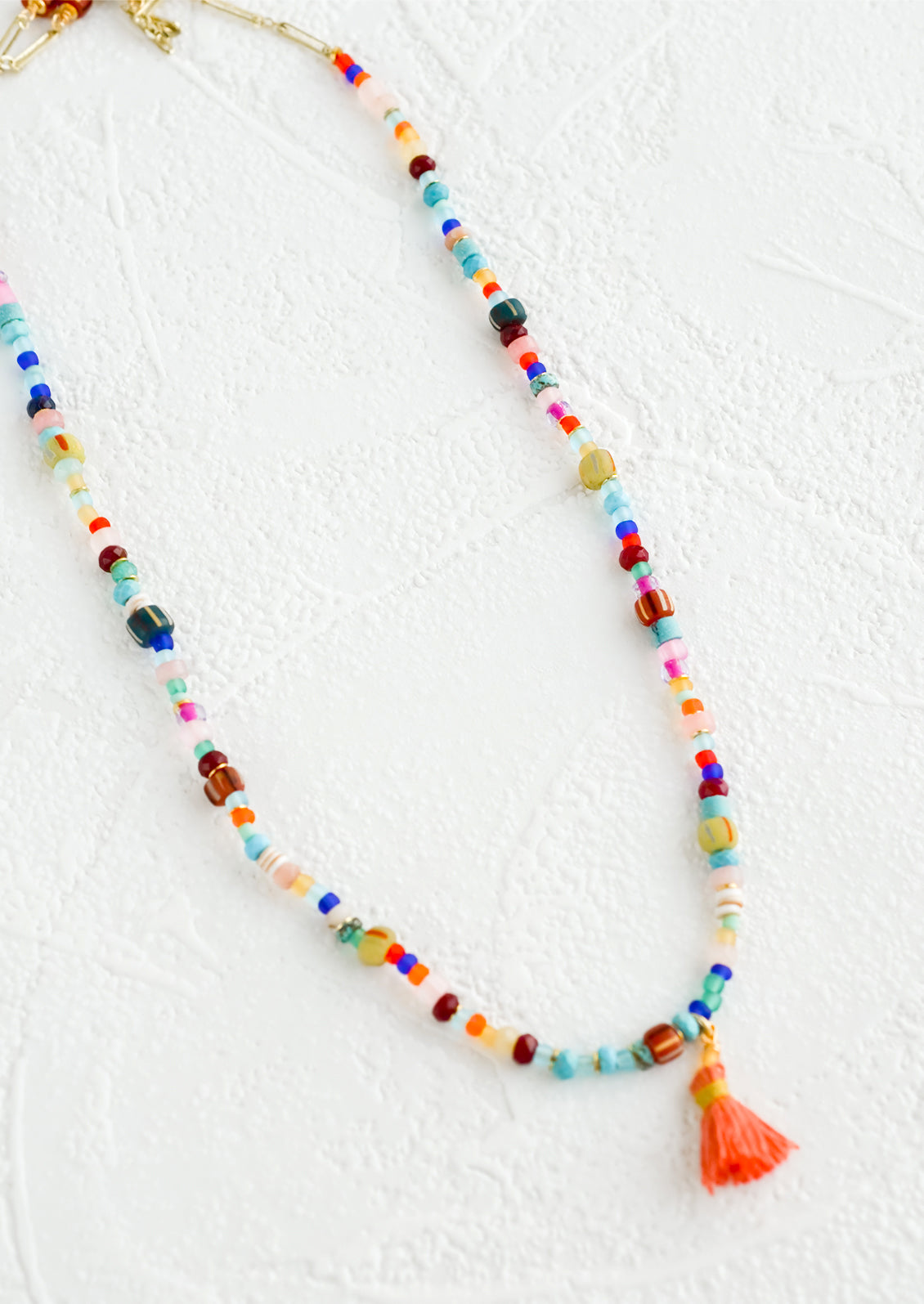 Colorful beaded necklace with peach tassel at center.