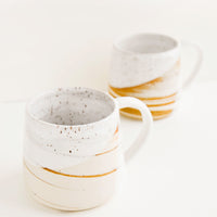 2: Two ceramic mugs with handles in swirled ivory and brown clay with speckled white glazed rim.