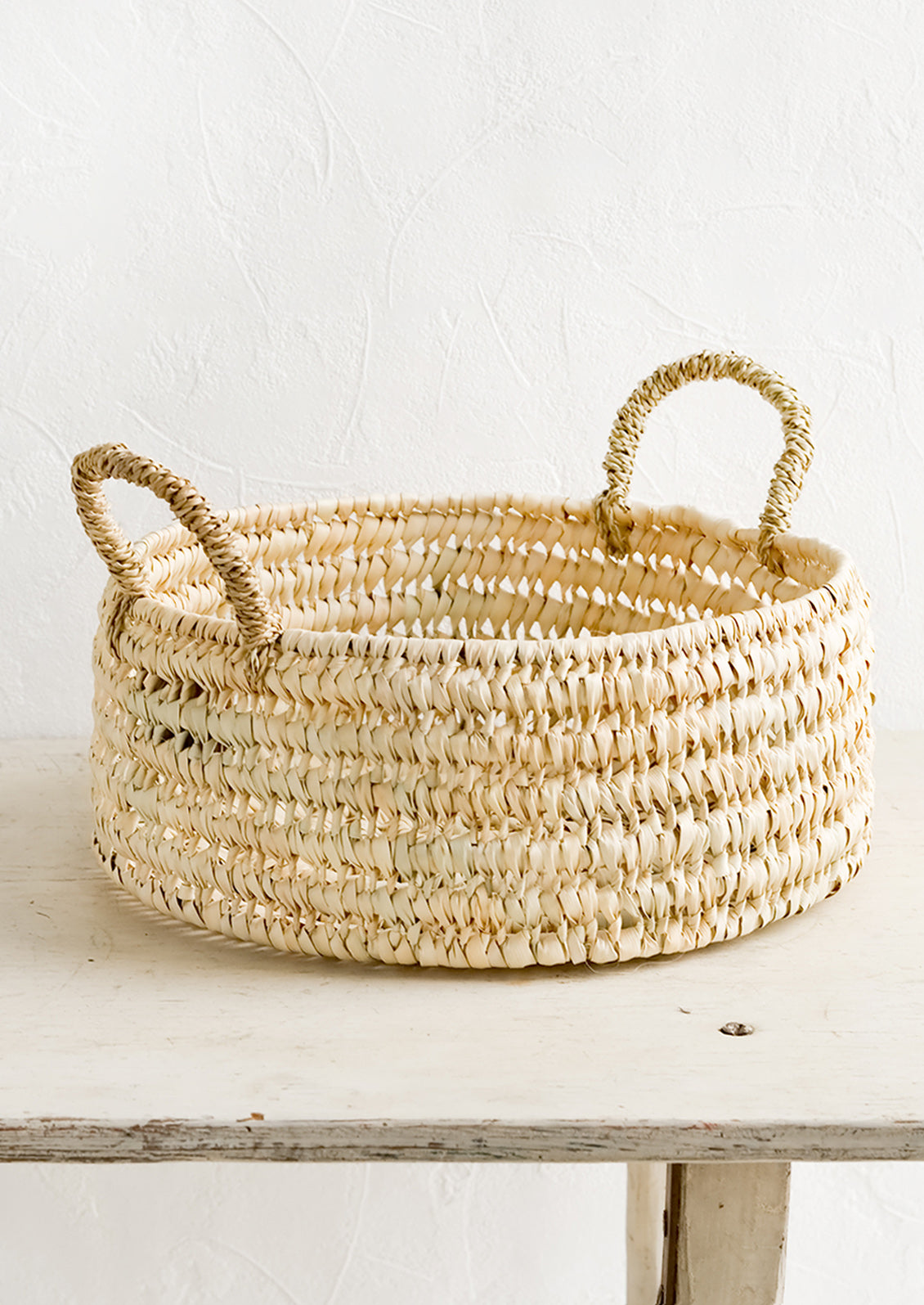 A round shallow storage basket made from dried palm leaf.
