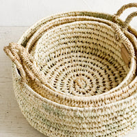 1: Three round palm leaf storage baskets in incremental sizes nested together.