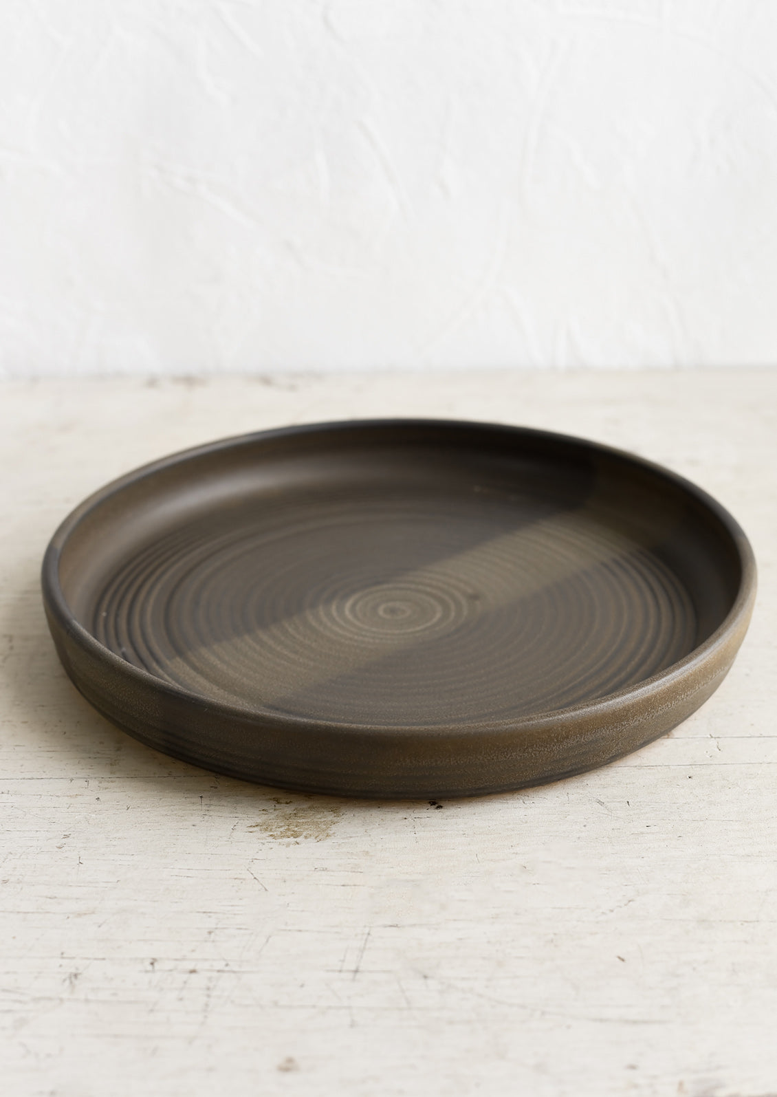 A shallow serving plate in matte dark brown.