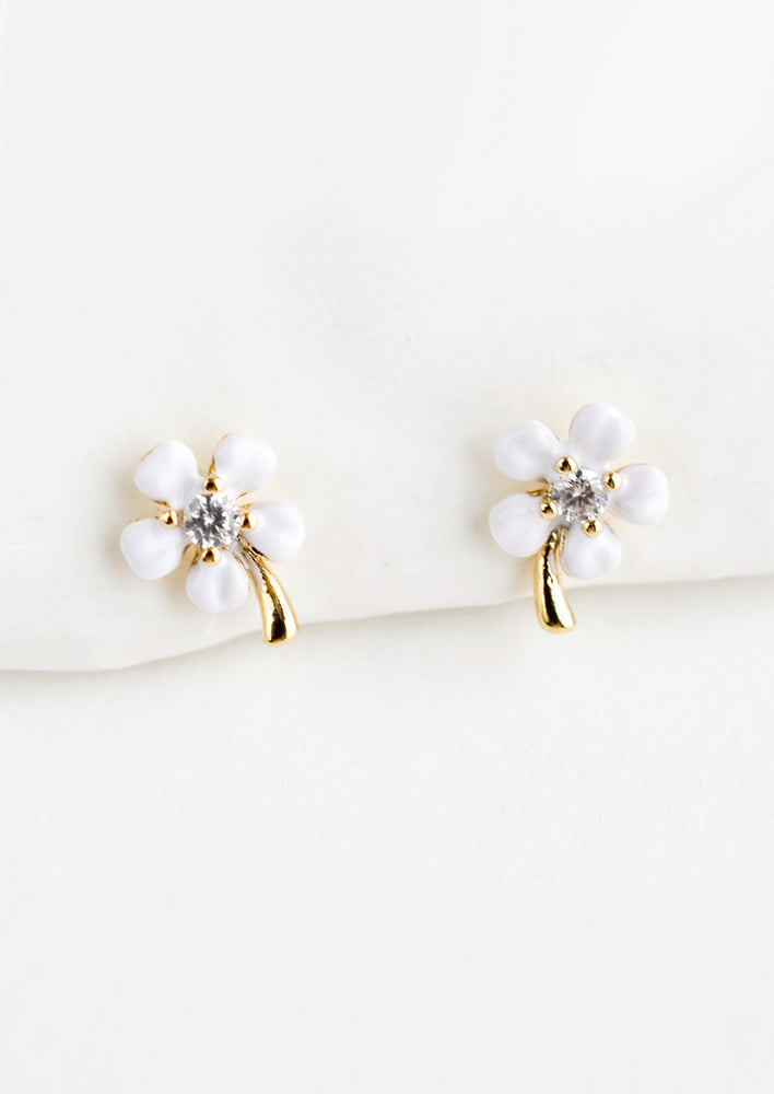 A pair of small gold stud earrings with white enamel flower and crystal center.