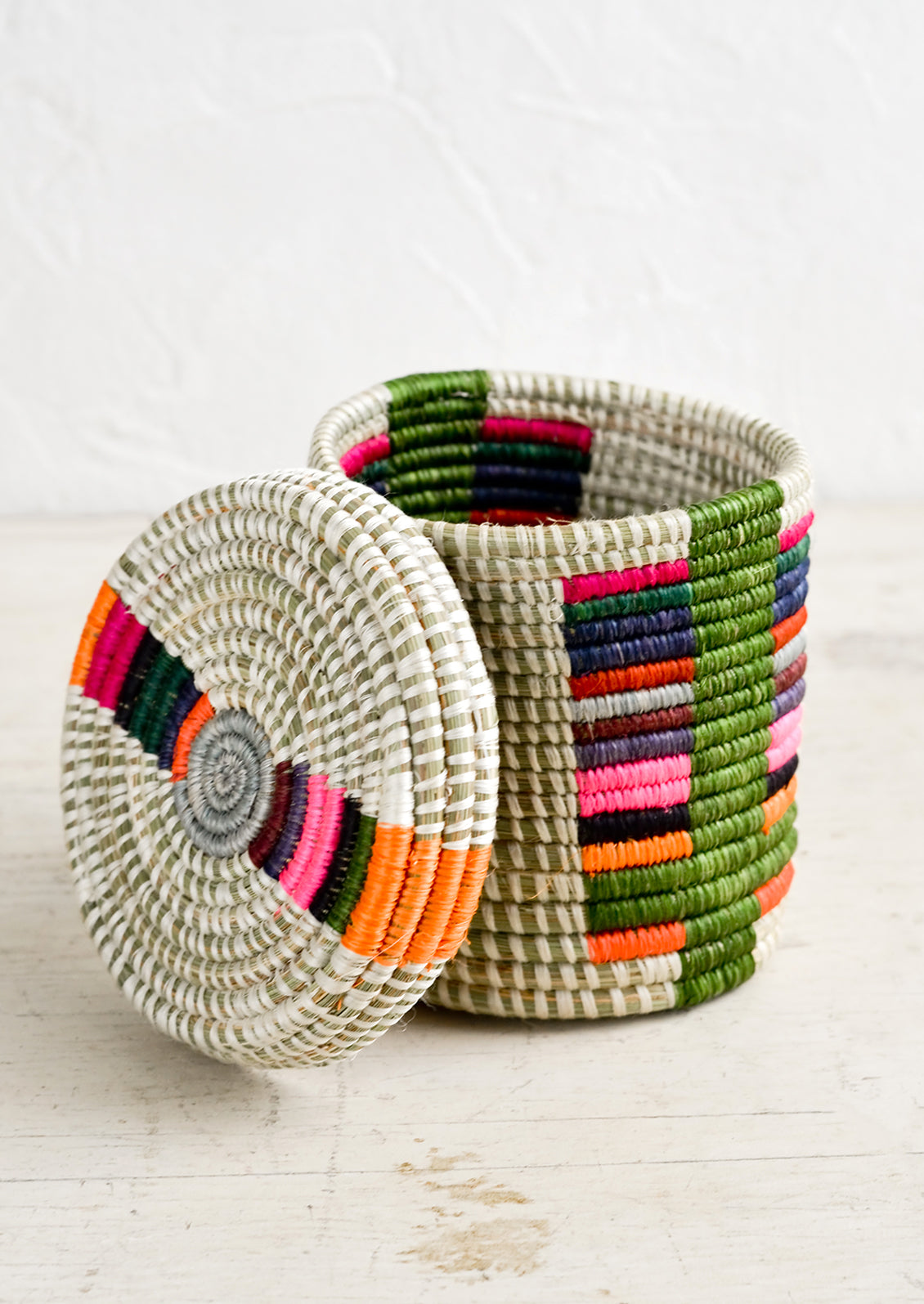 A small, round lidded basket made from woven sweetgrass on a table with lid askew.