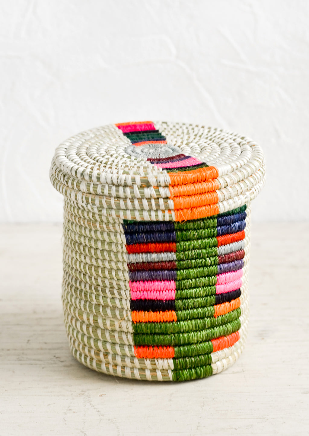 Chroma Multi: A small, round lidded basket made from woven sweetgrass with colorful line pattern.