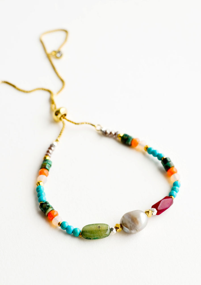 Gold chain bracelet with one pearl flanked by stone beads of blue, orange, green, and maroon.