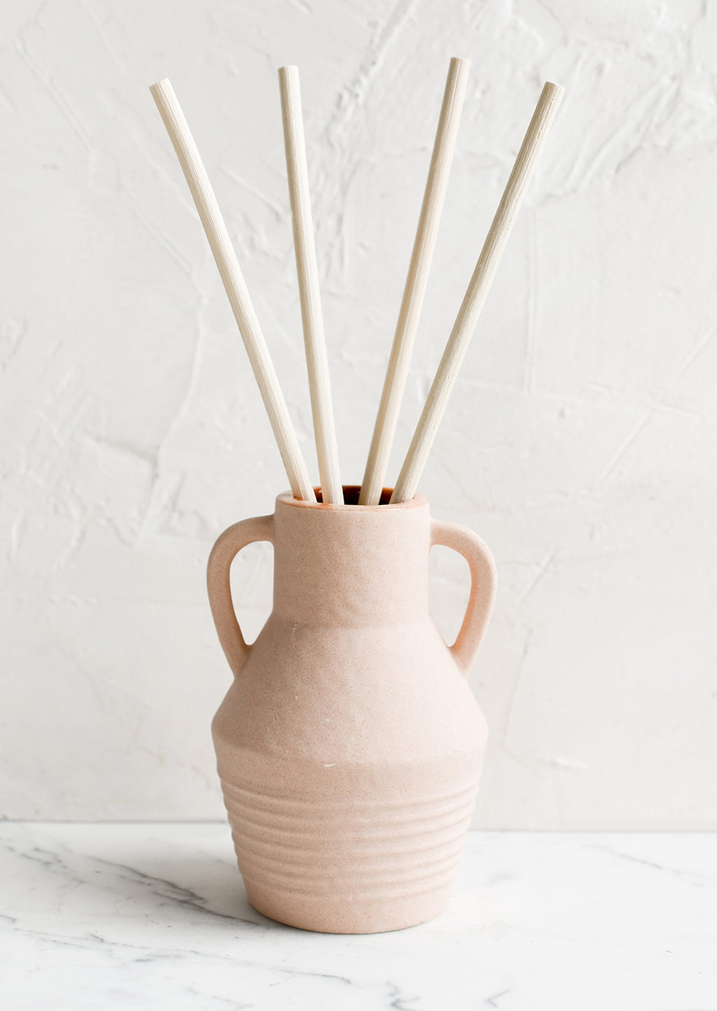 Black Fig & Olive: A ceramic reed diffuser bottle in peach.