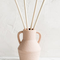 Black Fig & Olive: A ceramic reed diffuser bottle in peach.