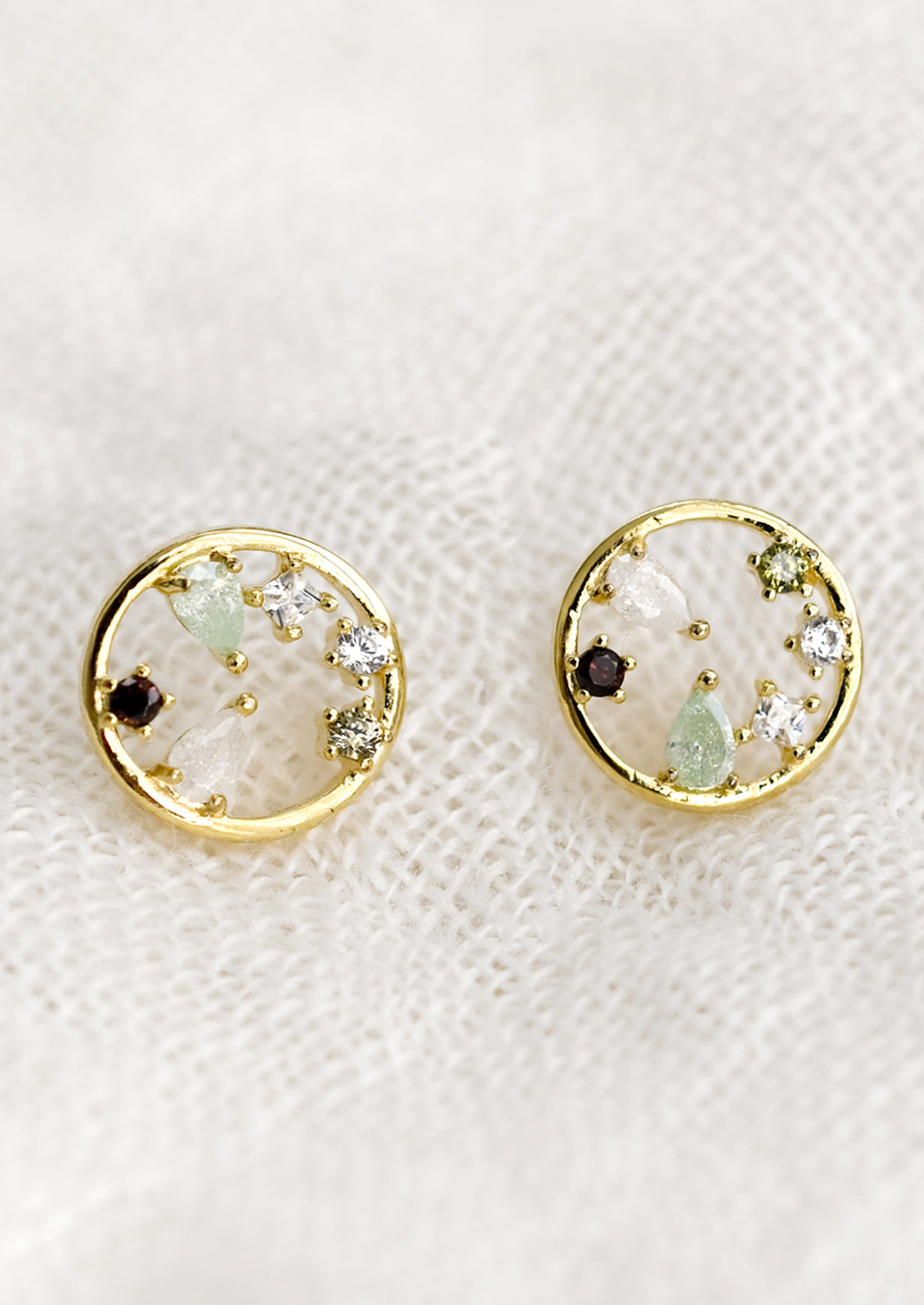 A pair of gold circular stud earrings with a mix of color and shape crystals inside the circle.