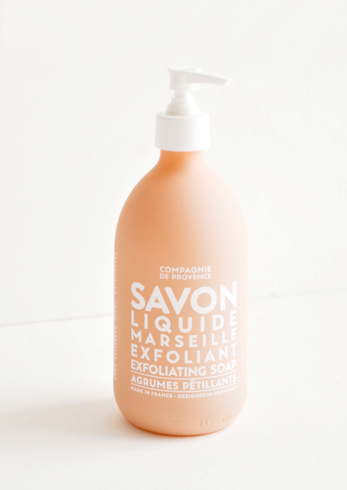 A matte glass peachy-nude soap bottle with a white plastic dispenser and white text.
