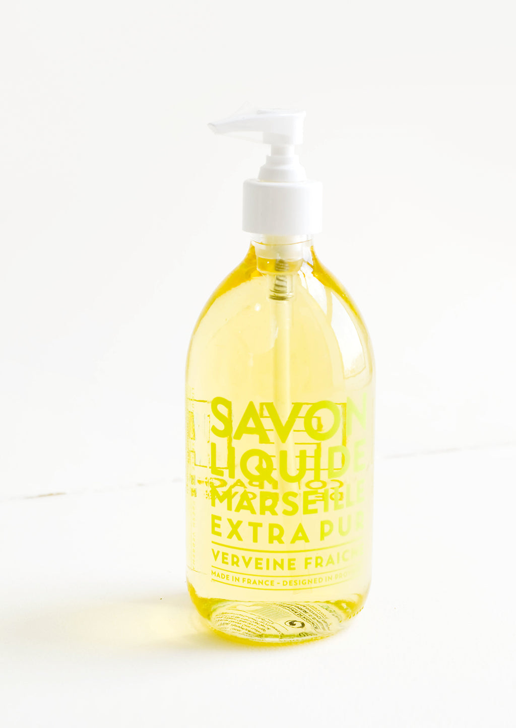 Verbena: A clear glass soap bottle with pale yellow interior liquid, lime green text, and a white plastic dispenser.