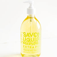 Verbena: A clear glass soap bottle with pale yellow interior liquid, lime green text, and a white plastic dispenser.