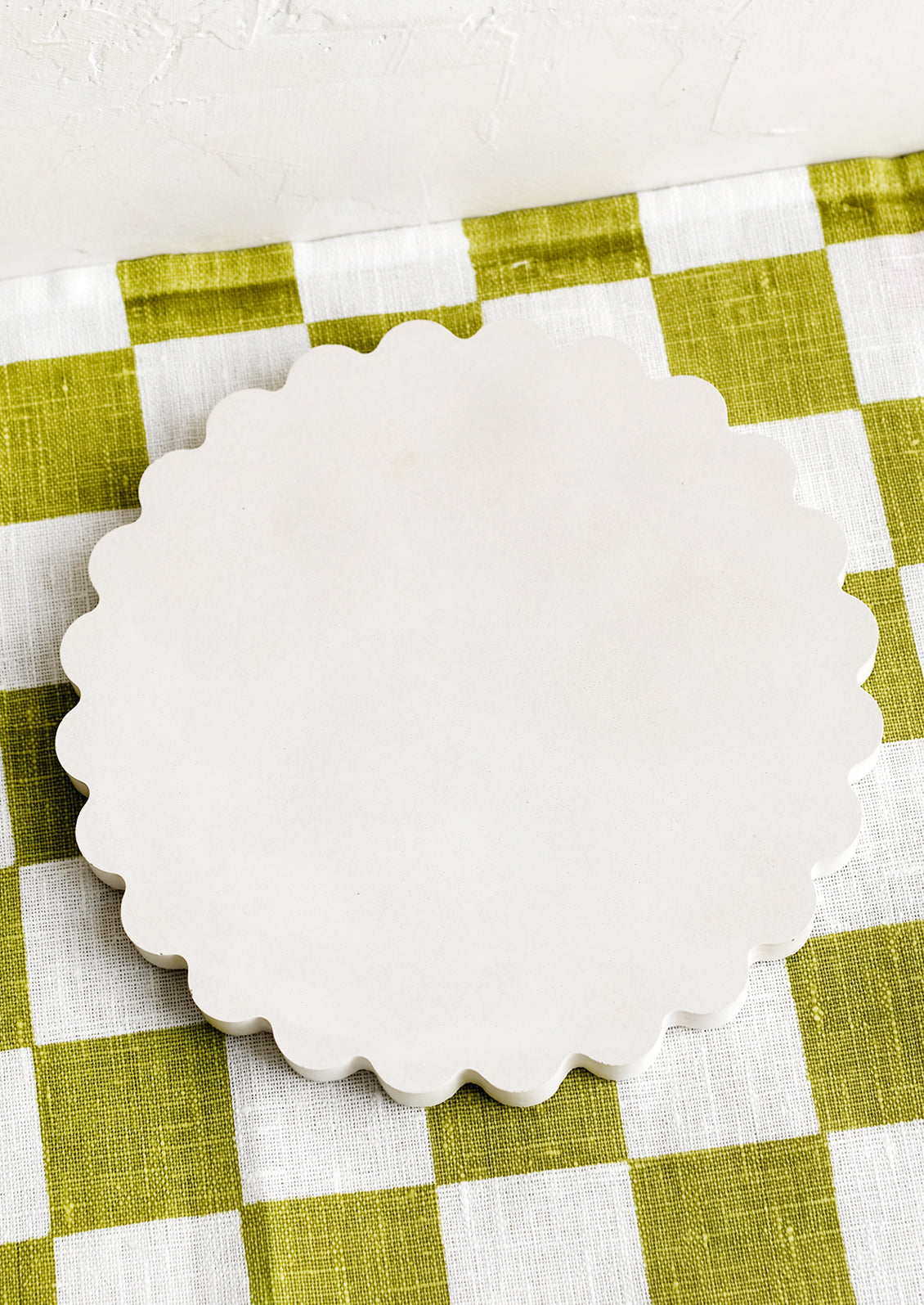 A concrete trivet with scalloped edges in cream.