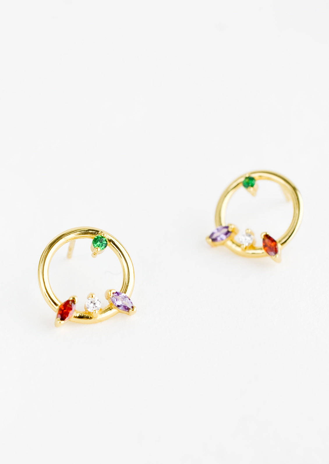 A pair of gold stud earrings in the shape of a circle with randomized colored crystal detailing.