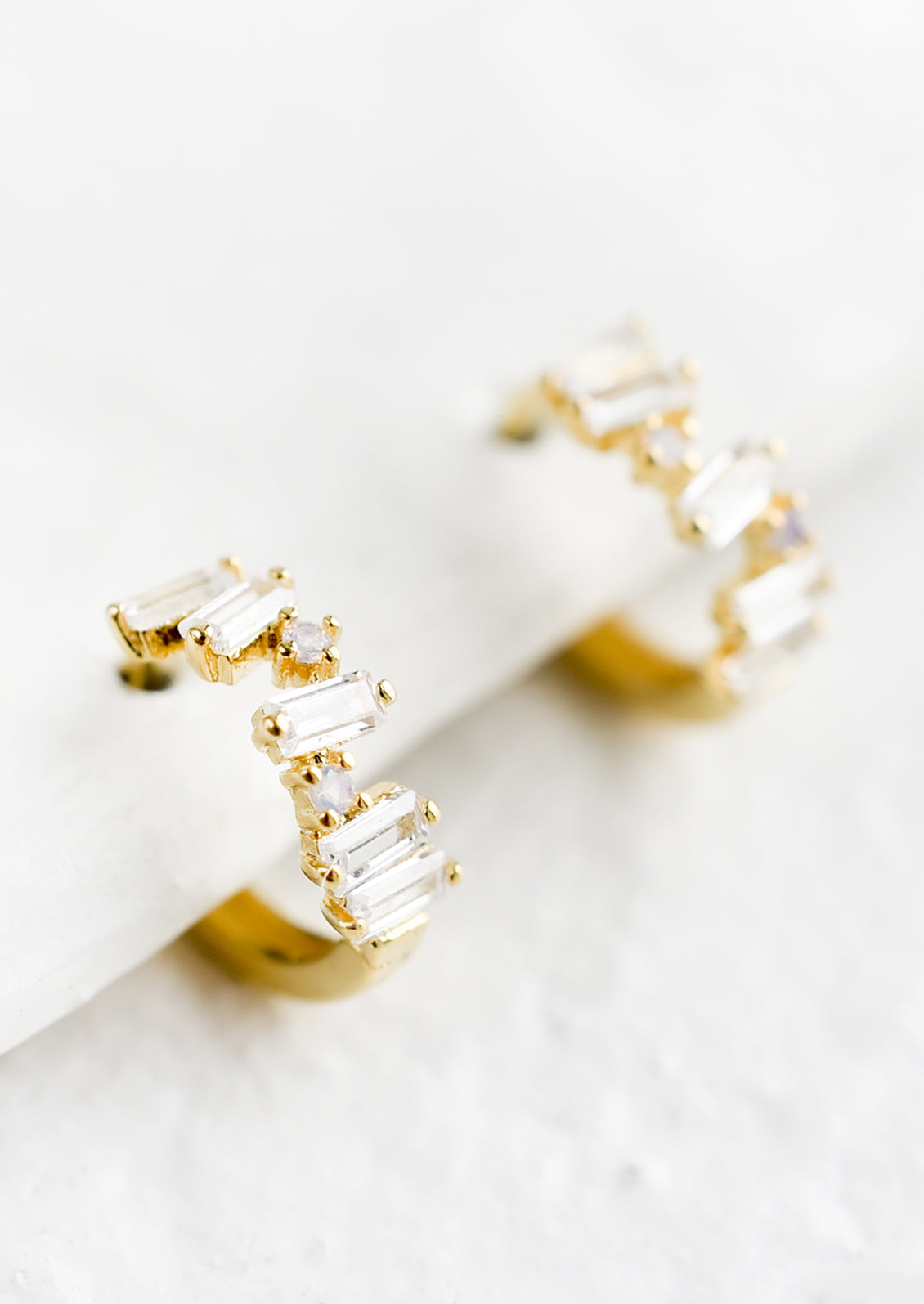 A pair of gold and crystal huggie hoop earrings with clear baguettes.