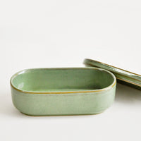 2: Oblong oval ceramic green Container with lid lying by its side.