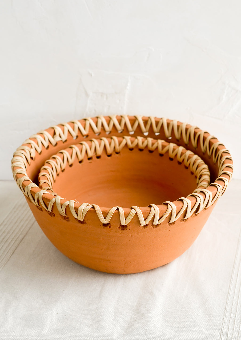 2: Nesting terracotta bowls with decorative woven seagrass trim around top.