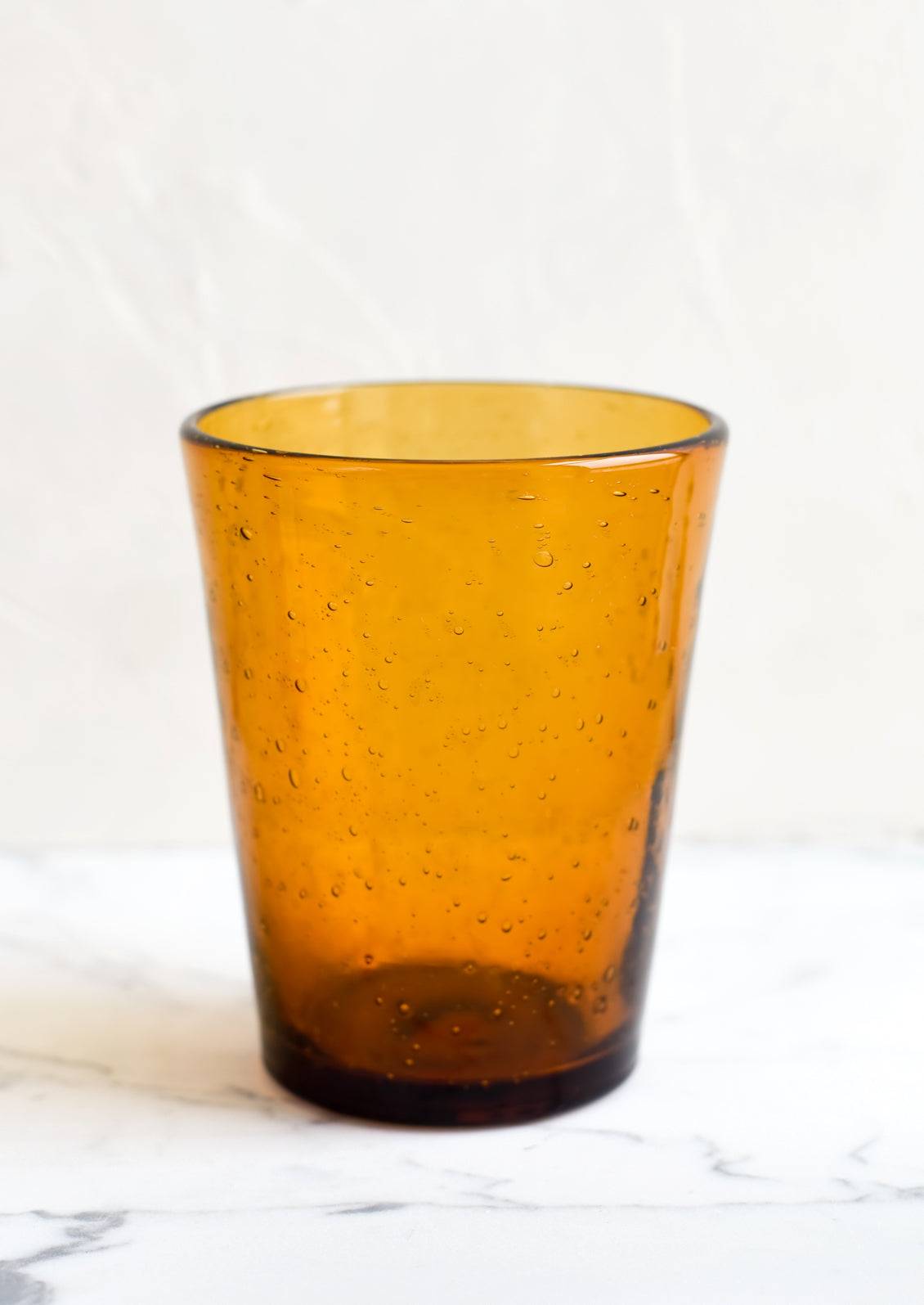 A glass tumbler cup in amber seeded glass.