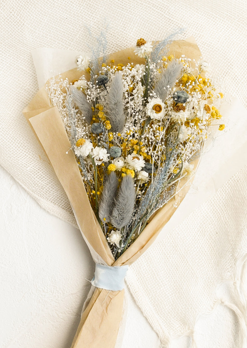 Full Size: A large bouquet of dried yellow, white and light blue flowers wrapped in parchment paper