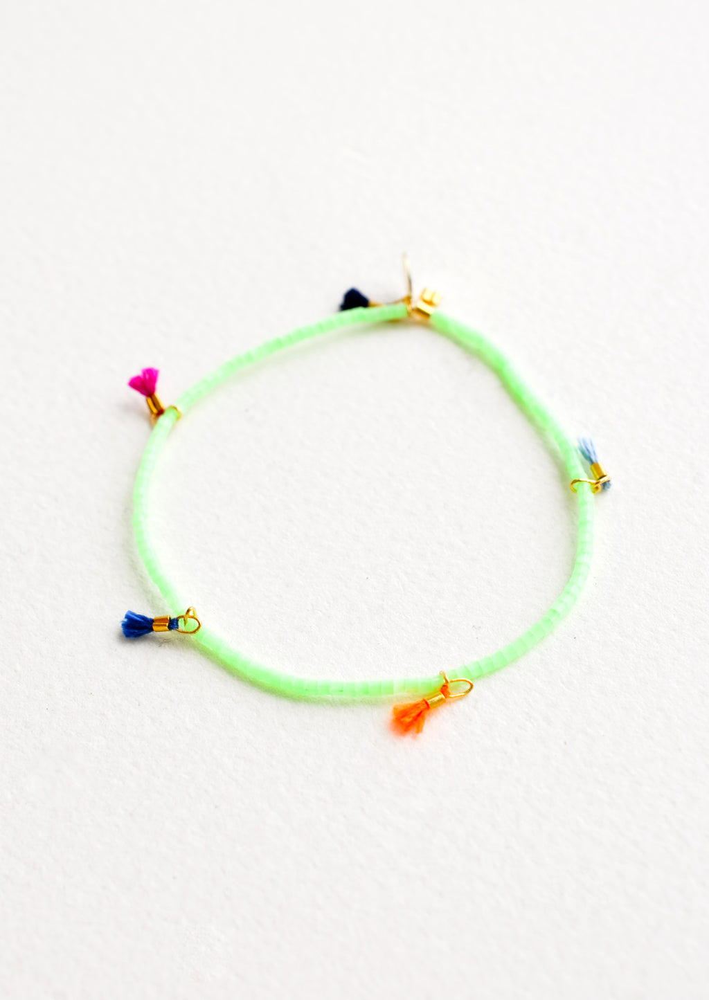 Mint Chip: Bracelet featuring green beads interspersed with 5 small multicolor string tassels on an elastic cord.