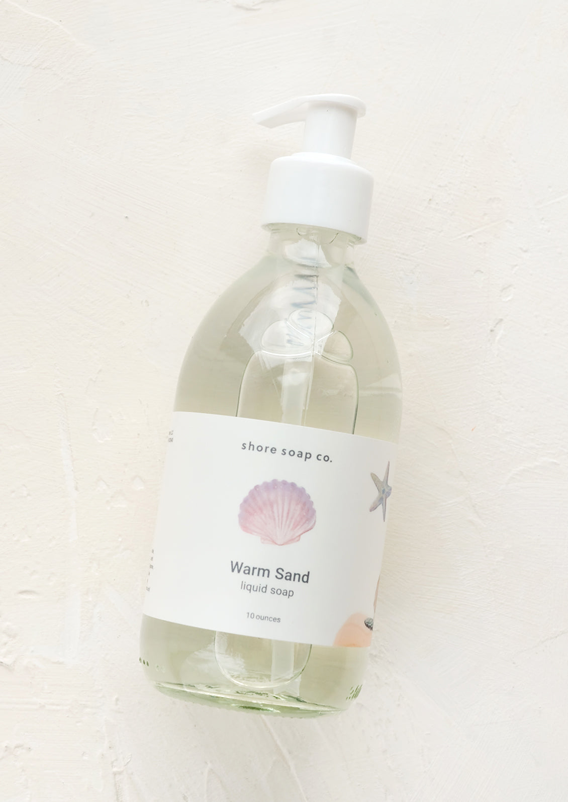 A glass pump bottle containing liquid soap in "Warm sand" scent.