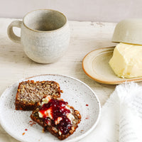 2: A breakfast tableware scene with coffee mug, butter dish and toast and jam on a ceramic plate.