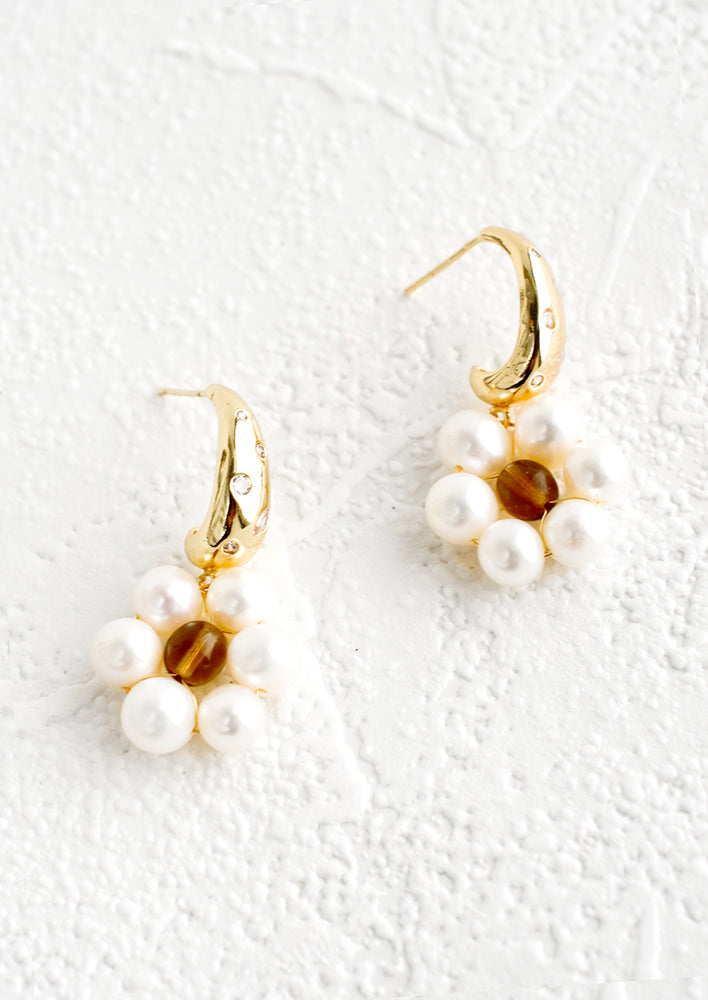 A pair of earrings with a crystal studded half-hoop top, and a flower shape made out of pearls.