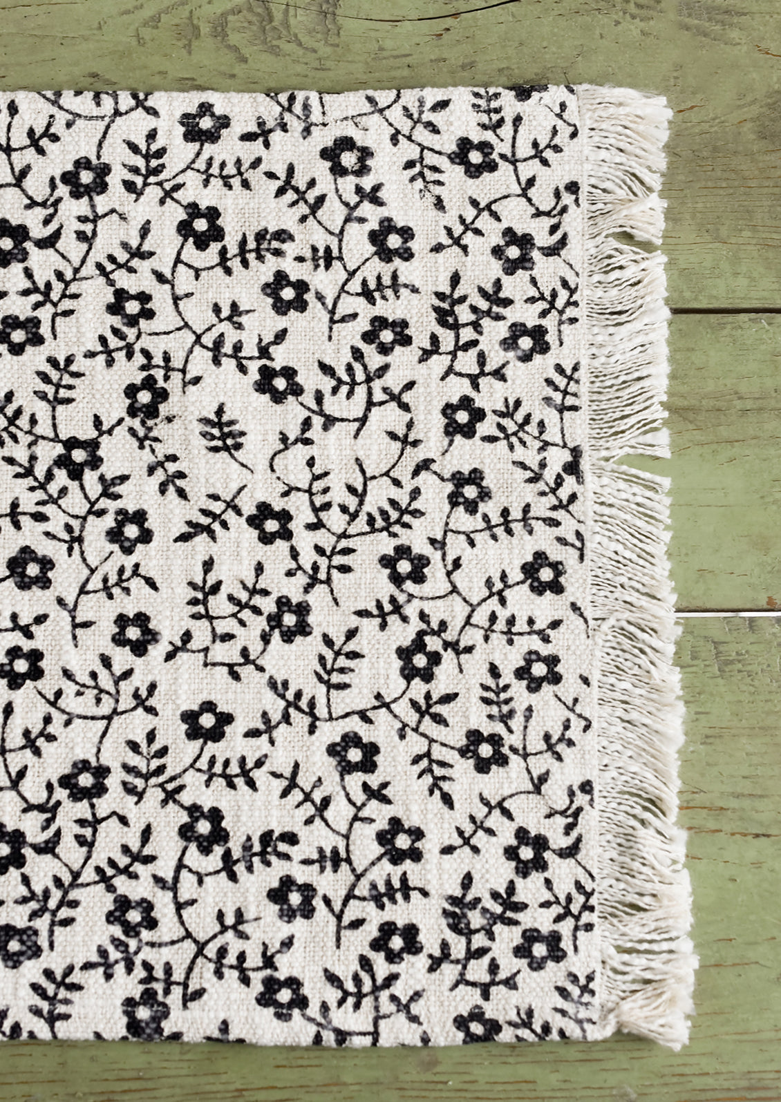 A black and white floral print placemat with fringe trim.