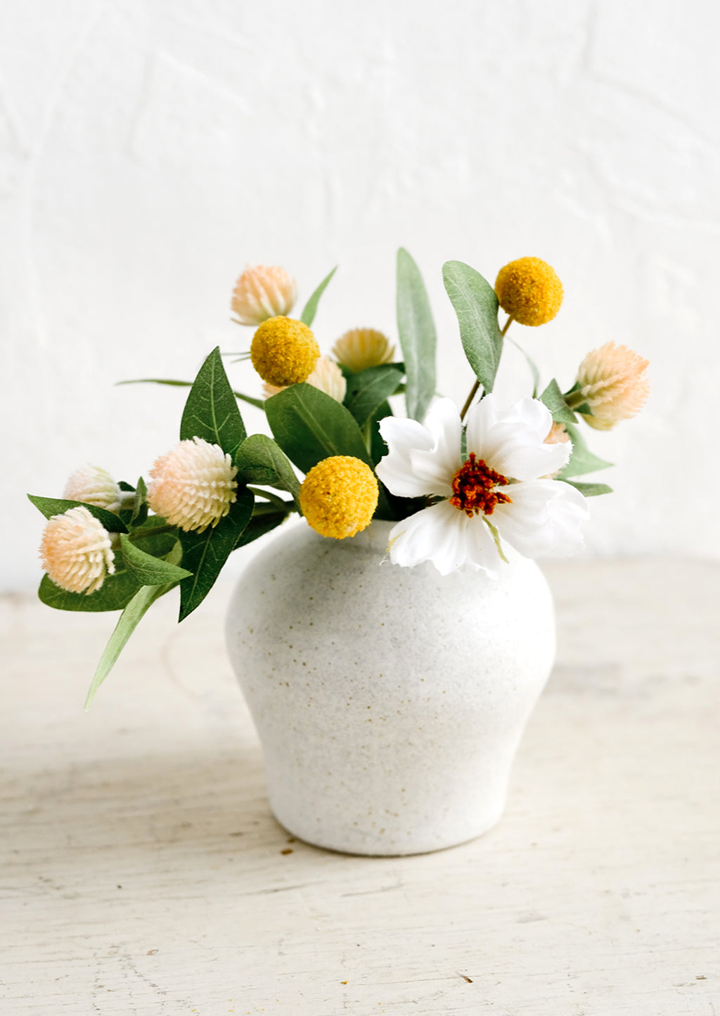 2: A small white ceramic vase in curvy shape with colorful flowers.