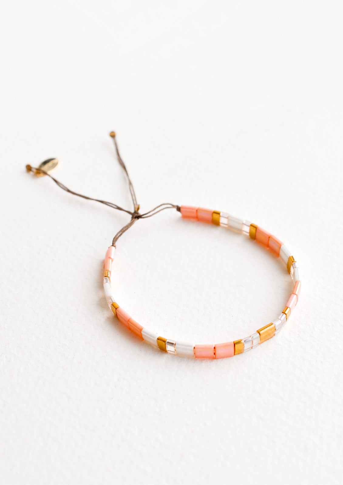 Bracelet featuring flat peach and white glass beads interspersed with flat gold bead on an adjustable cord.