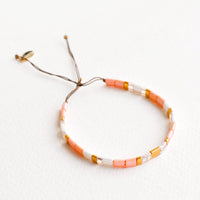 Peach: Bracelet featuring flat peach and white glass beads interspersed with flat gold bead on an adjustable cord.