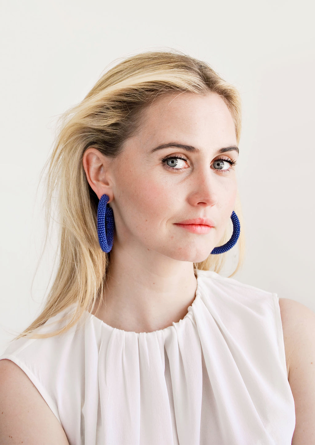 2: Model wears blue beaded hoop earrings and white blouse.