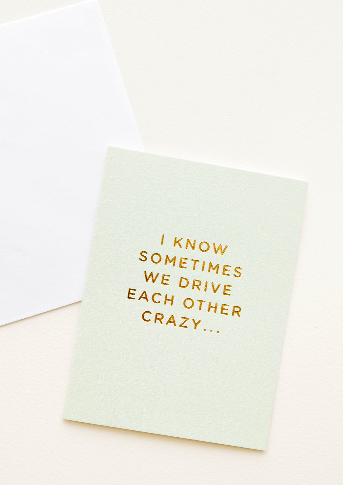 A pale green greeting card with script reading "I know sometimes we drive each other crazy" in gold foil.