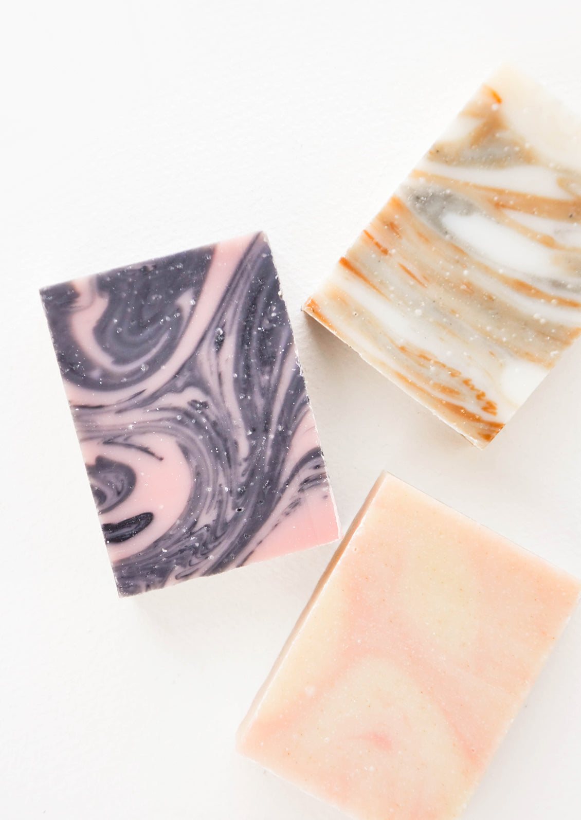 Three marbled bar soaps in black and pink, pink and beige, and white and orange.