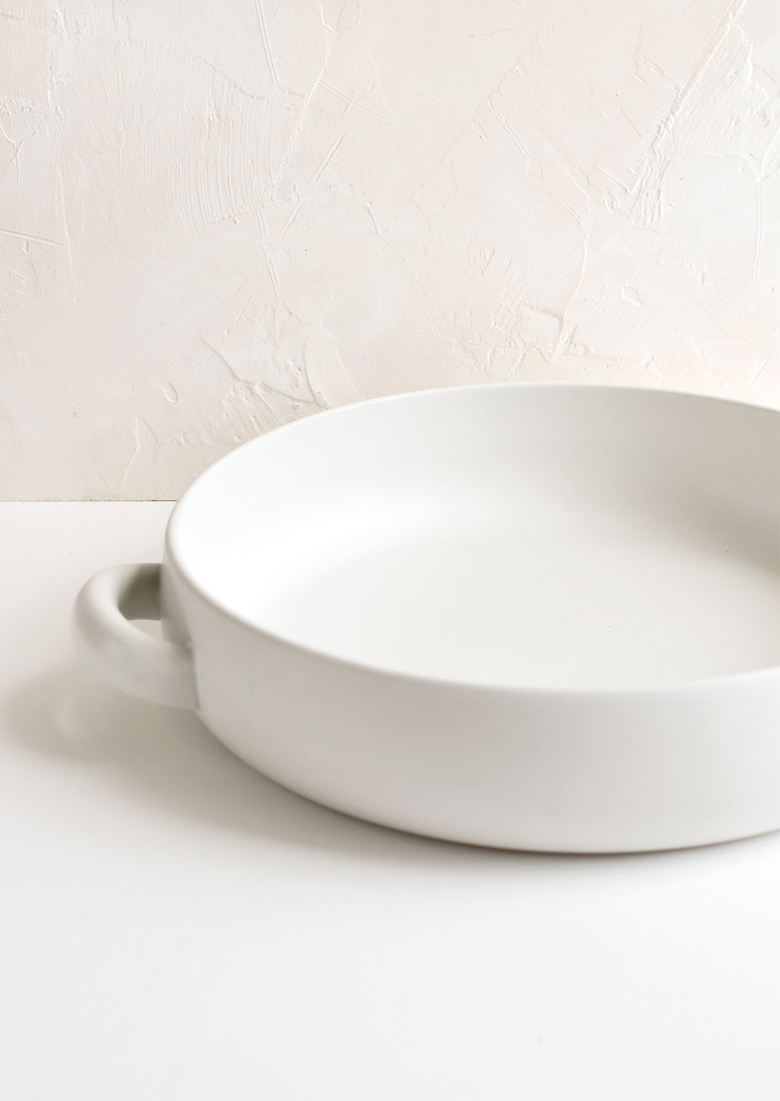 A round, shallow extra large serving bowl in white ceramic with curved handles at sides.