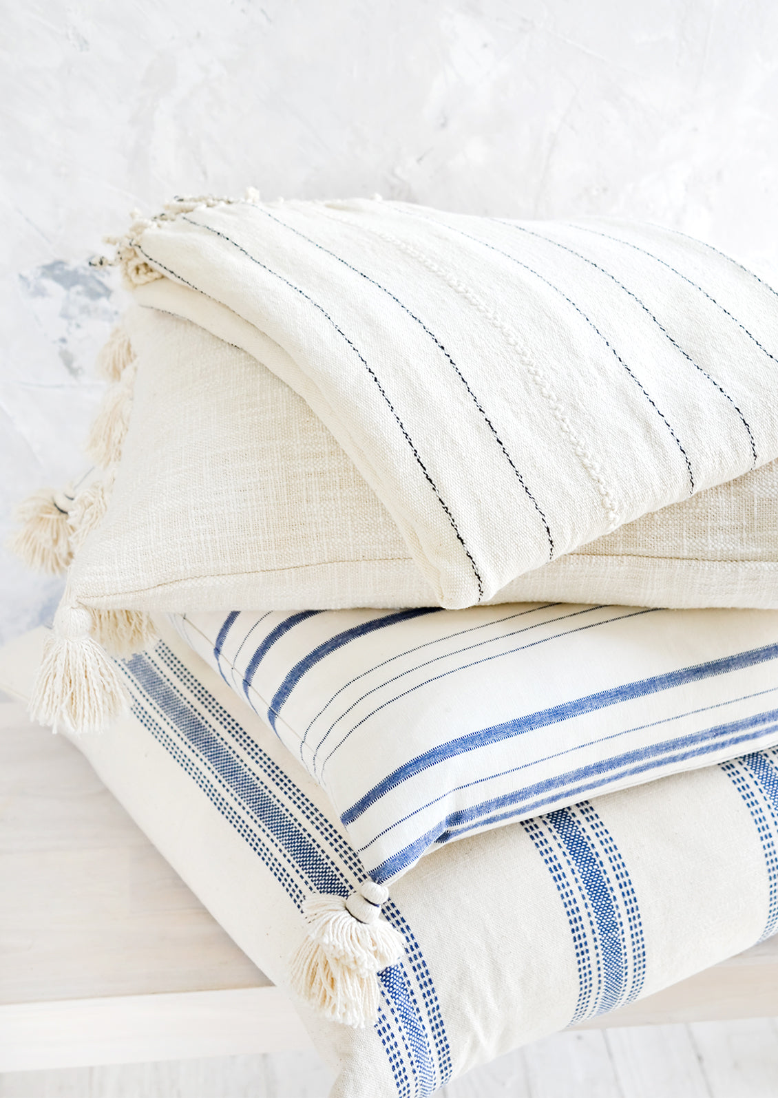 A stack of pillows and blankets in blue, white and cream colors.