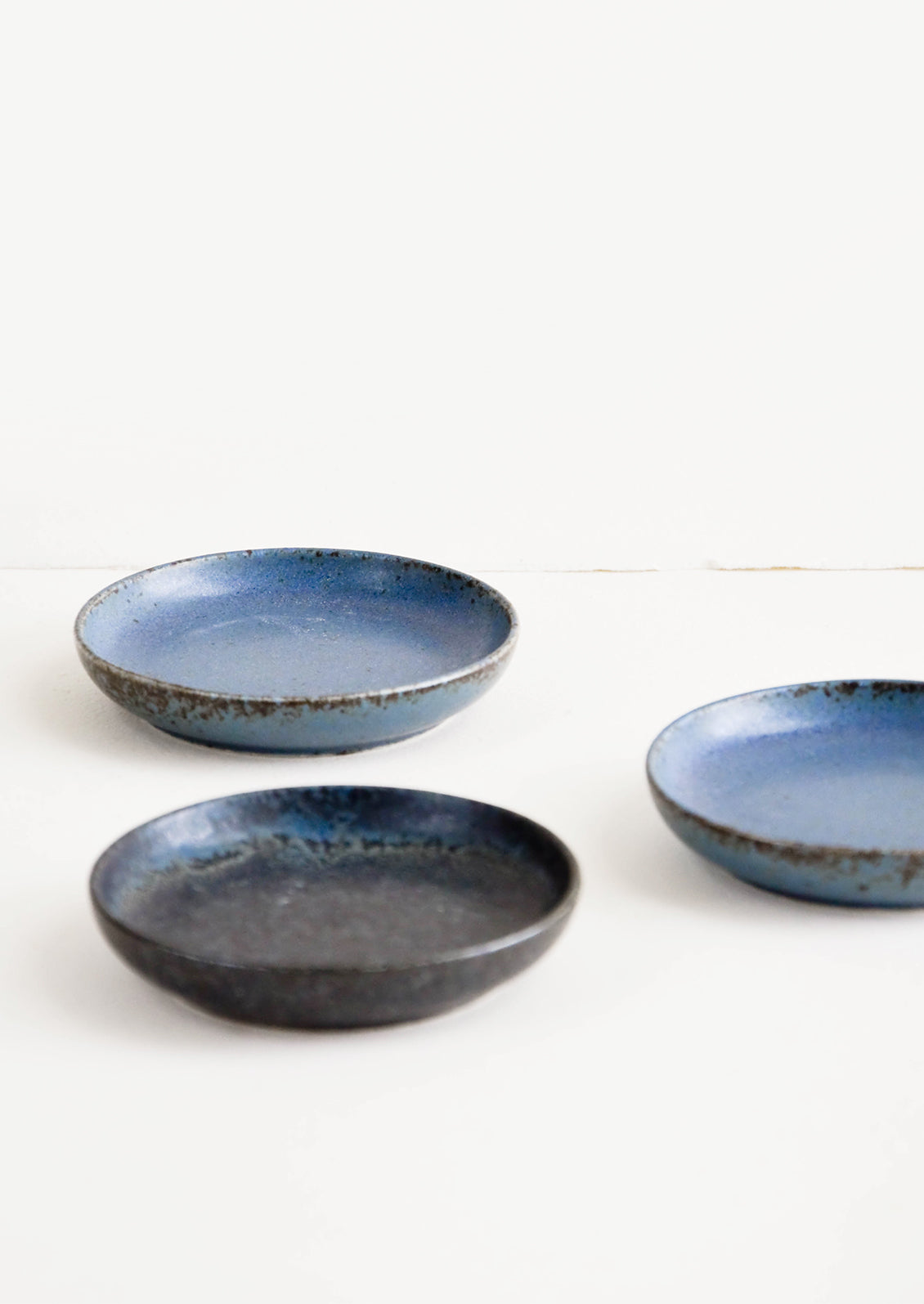 Small, round ceramic plates in a rustic matte glaze in blue and black