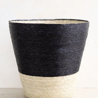 Carbon: A conical shaped storage basket made from woven palm leaf in black & natural color way.