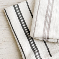 1: Two striped cotton hand towels in black and taupe colorways.