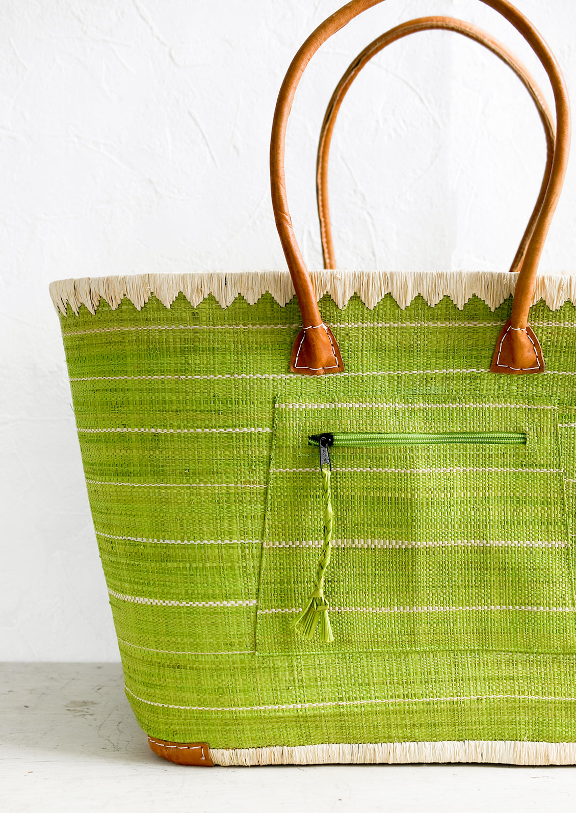 A raffia tote bag in green stripes with leather handles.
