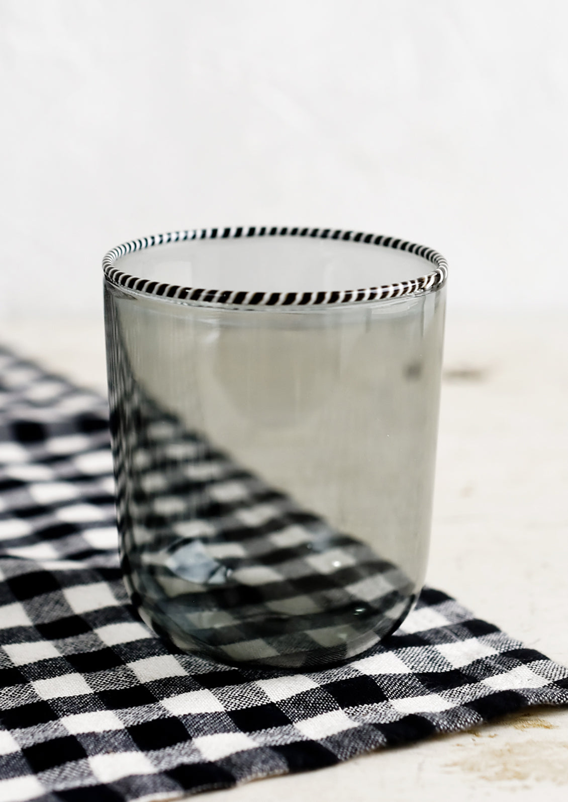A transparent glass tumbler in grey color with black and white striped rim.