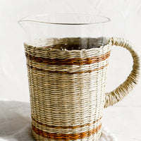 1: A glass pitcher with striped seagrass cloak and handle.
