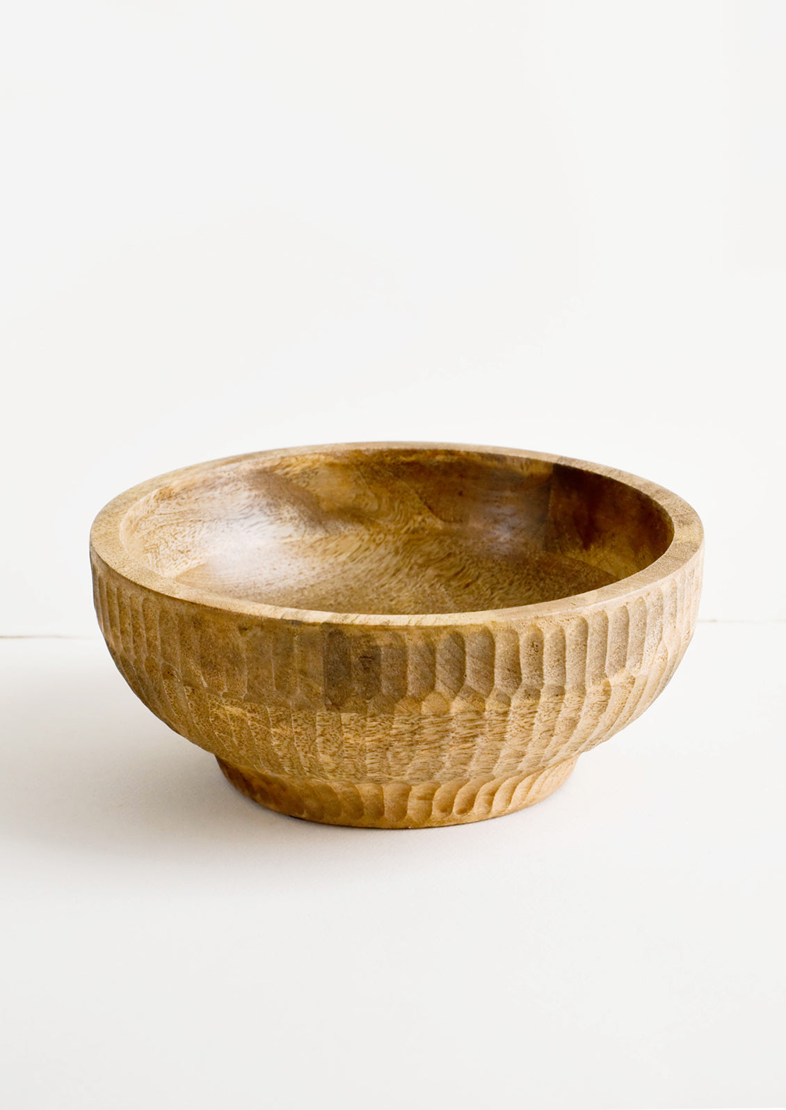 Round mango wood bowl with footed silhouette and carved detailing on exterior