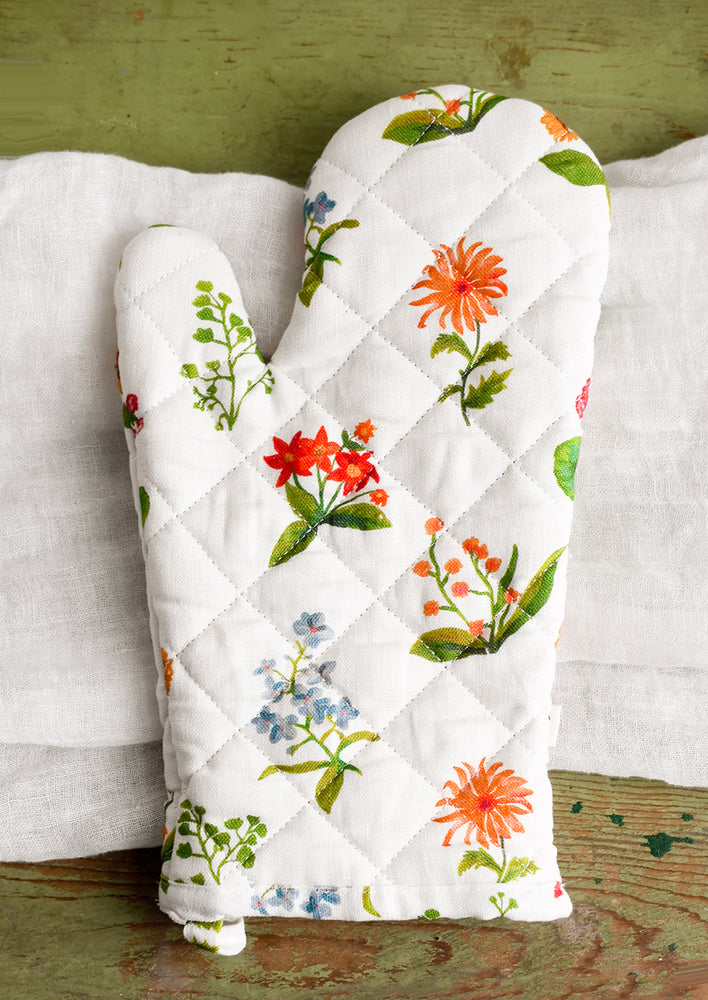 A quilted white oven mitt with multicolor flower print.