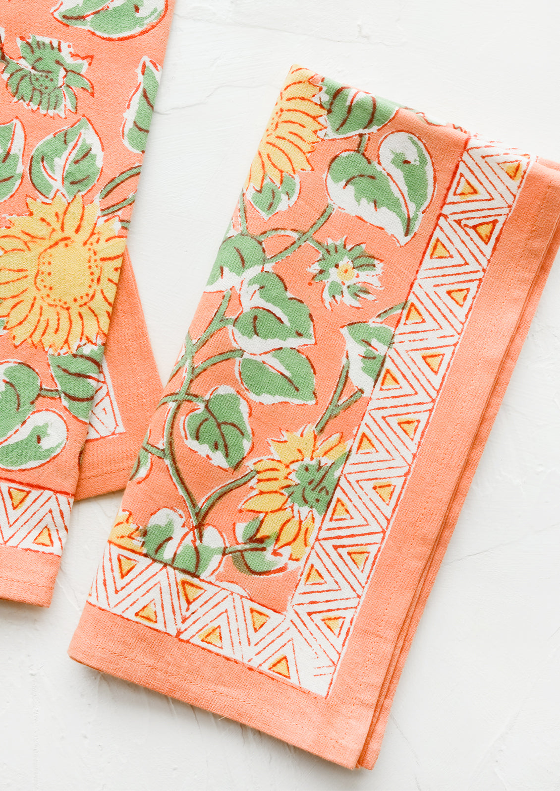Pair of peach cotton napkins with yellow and green sunflower print.