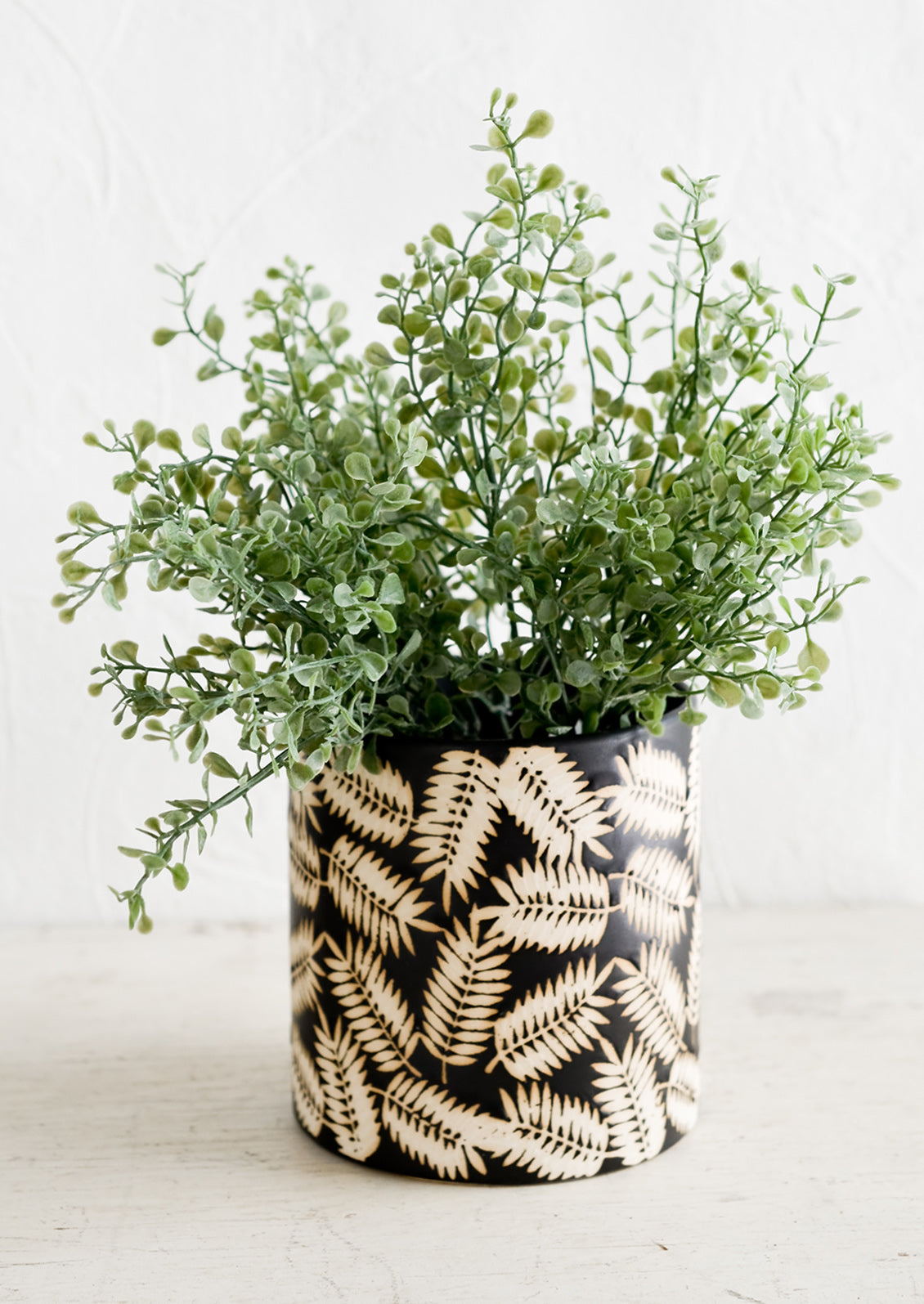 A ceramic planter with palm leaf print, housing green plant.