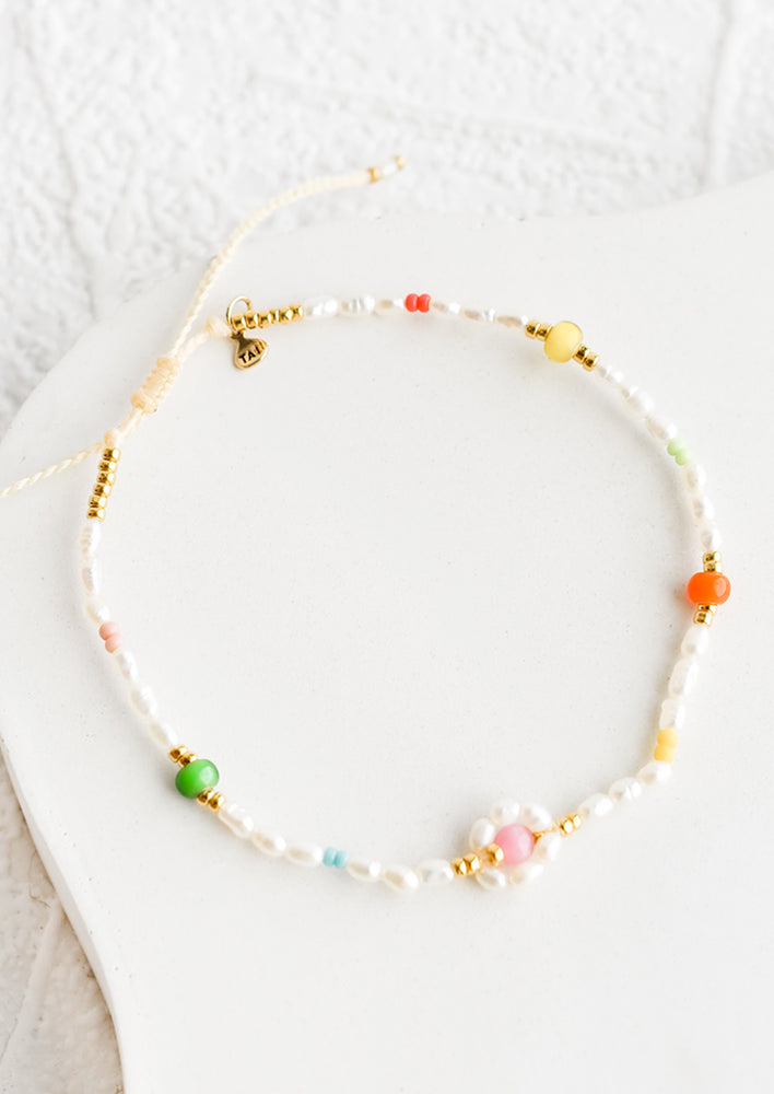 A pearl bracelet with small rainbow colored beads and beaded flower detail.