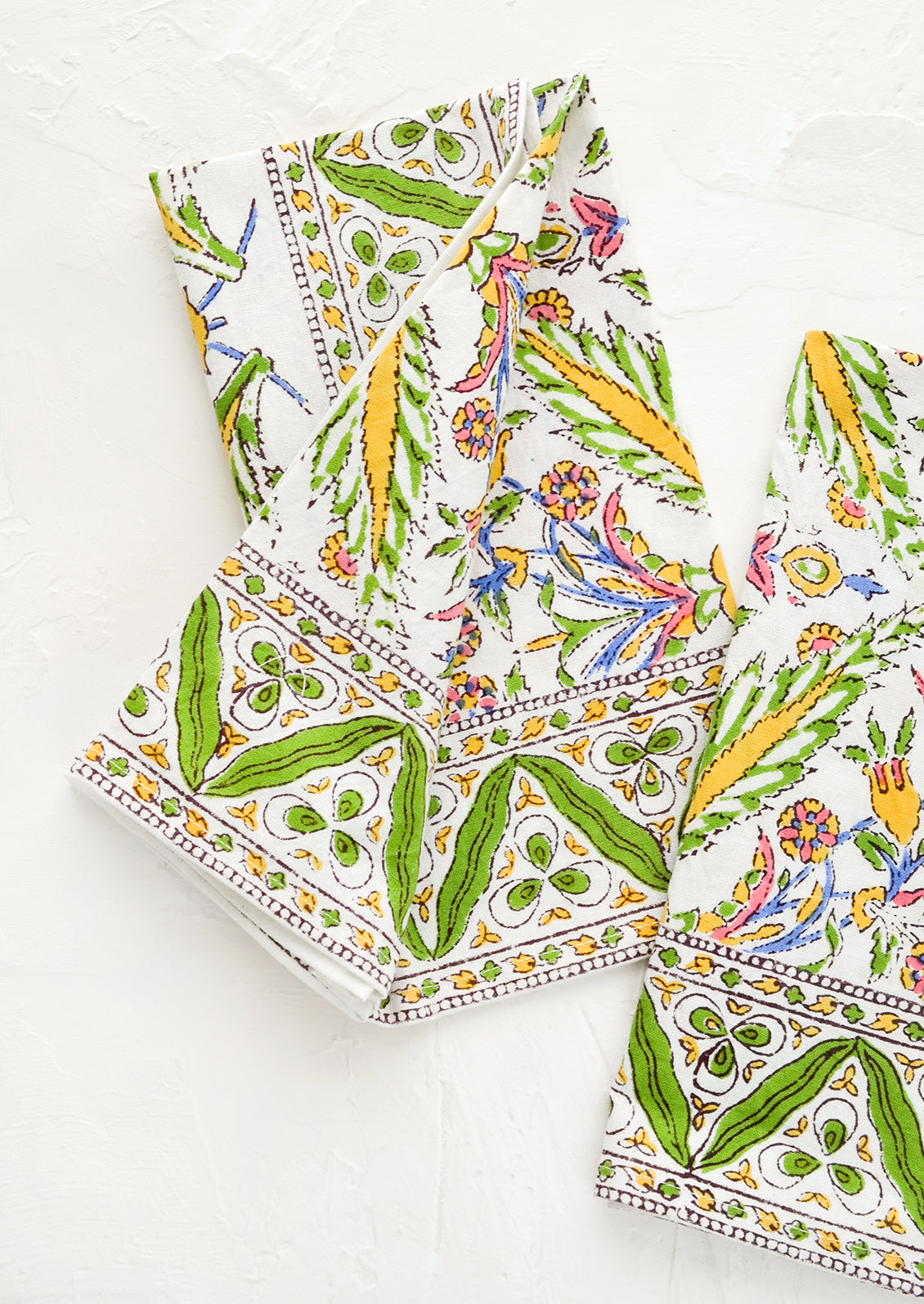 A block printed pair of napkins in green, yellow, blue and pink pattern.